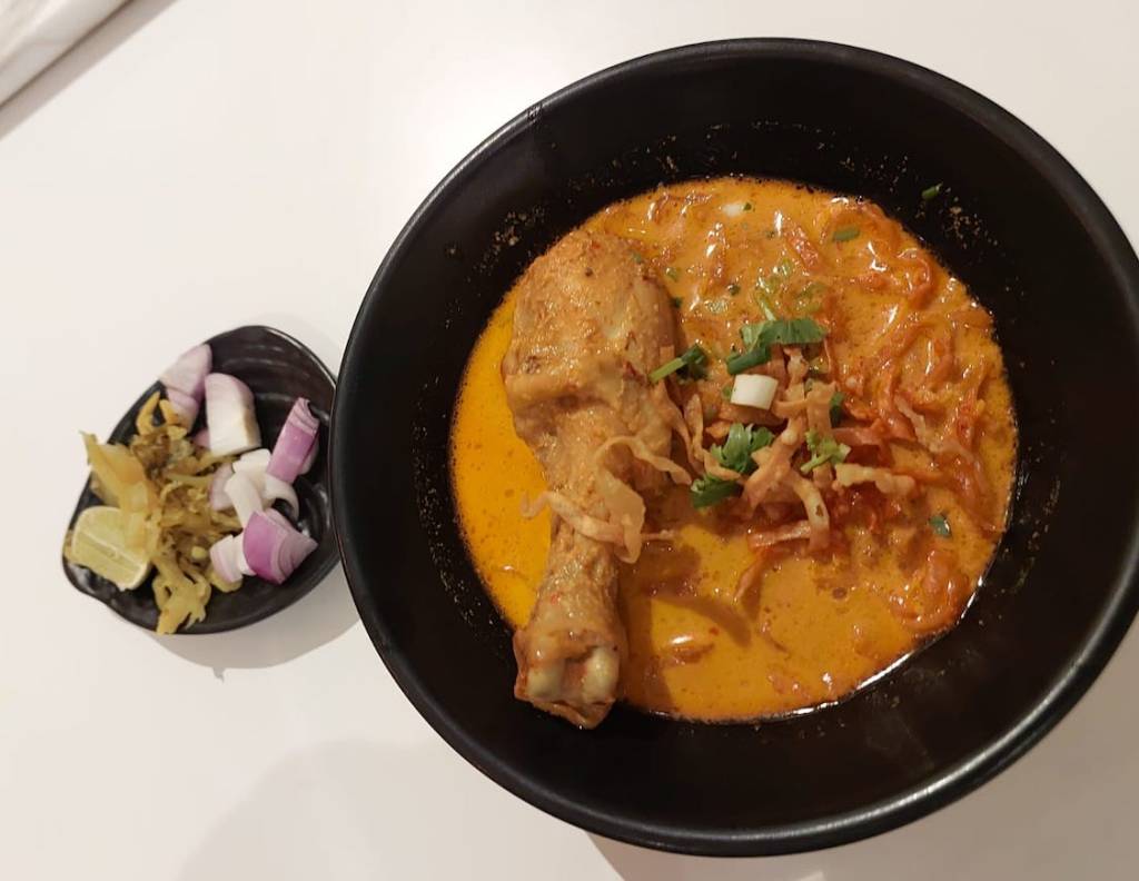 photo-of-thai-curry-in-black-bowl-with-a-chicken-drumstick-and-onion-and-pickles-next-to-it